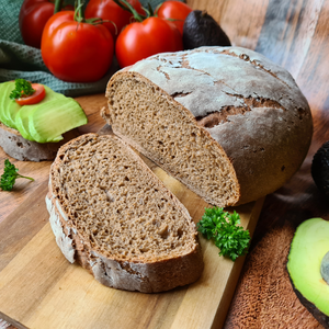 Fitnessfoodieontour hat unsere Brotbackmischung gebacken und ein wunderschönes Brot auf einem Holzbrett angerichtet. Serviert wird eine Scheibe Brot belegt mit Avocado, Petersilie und einer Scheibe Tomate. 